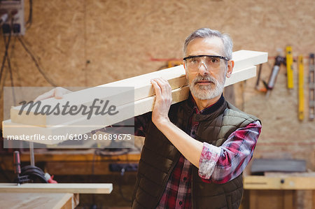 Portrait of a carpenter holding wood plank on his shoulder in a workshop