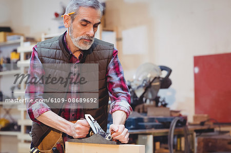 Portrait of carpenter perfecting wood plank form with a work tool in his workshop