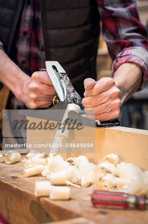 Portrait of carpenter perfecting wood plank form with a work tool in his workshop