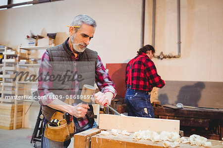 Carpenter perfecting wood plank form with a mallet in his workshop