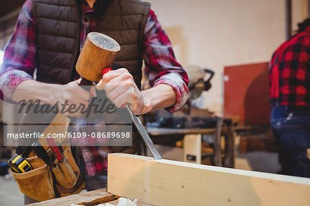 Close-up of carpenter using a mallet on a wood plank in his workshop