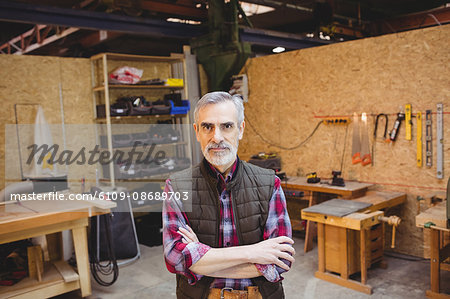 Senior carpenter crossing arms while looking at camera in his workshop Senior carpenter crossing arms while looking at camera in his workshop