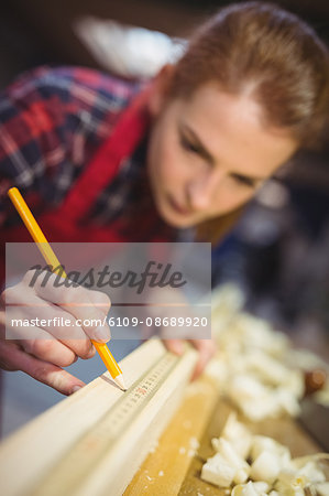 Female carpenter marking on wooden plank with pencil in workshop