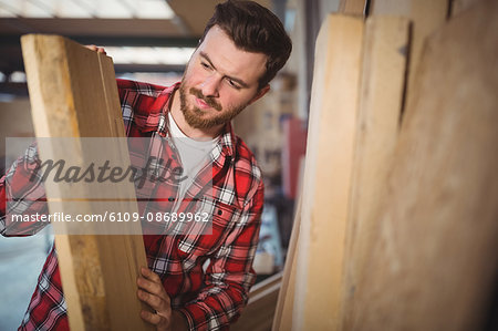 Carpenter looking at wooden plank in workshop