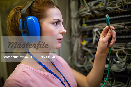 Technician in head phones looking at patch cable in server room