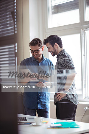Happy businessman with colleague using digital tablet in creative office seen through glass