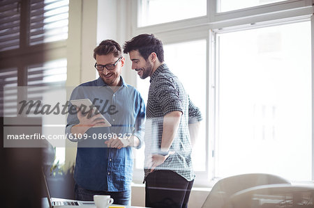 Smiling businessman with colleague using digital tablet in creative office seen through glass