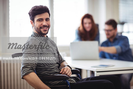 Smiling businessman on wheelchair with coworkers at creative office