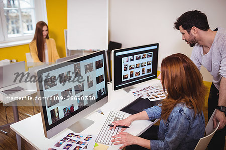 Female photo editor with coworkers working on computers in creative office