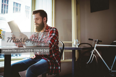 Young male customer reading from tablet while sitting at cafeteria