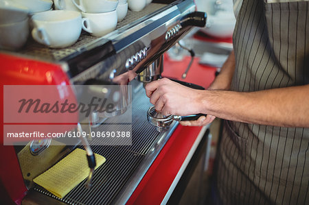 Midsection of waiter with strainer by espresso maker at cafe