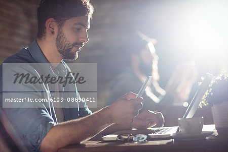Side view of handsome young man using cellphone and laptop at cafe