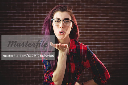 Young woman giving a kiss on the hand against brick wall