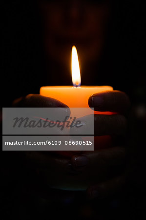 Cropped image of fortune teller holding lit candle in darkroom