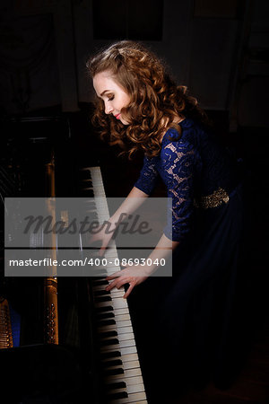 Young woman musician standing in front of grand piano and plays music.