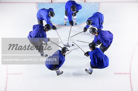 Hockey players in blue uniforms huddling around puck on ice