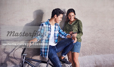 Teenage couple with BMX bicycle texting with cell phone at wall