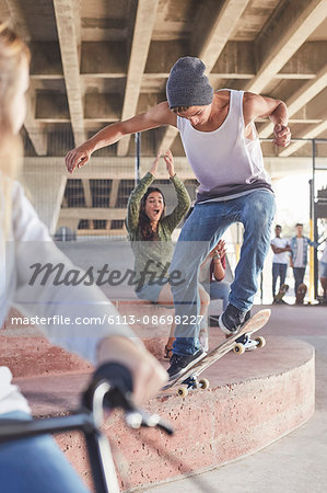 Friends watching teenage boy skateboarding at skate park