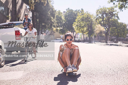 Teenage girl sitting riding skateboard on sunny urban street