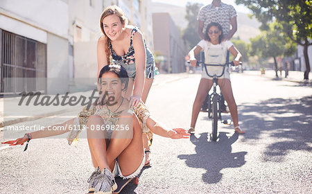 Teenage girls riding skateboard and BMX bicycle on sunny urban street