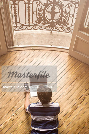Man lying on floor using laptop and smartphone
