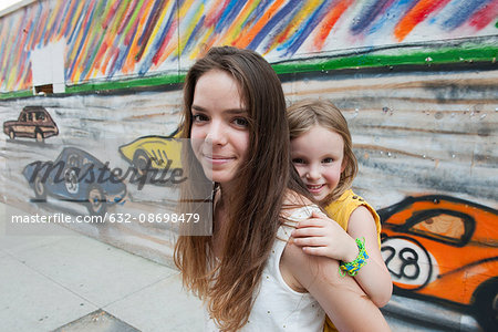 Teenage girl giving her little sister a piggyback ride, portrait
