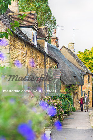 England, Gloucestershire, Chipping Campden. A couple walking past thatched cottages in the village.