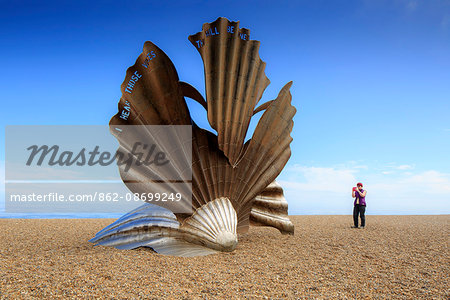 England, Suffolk, Aldeburgh. Tourist taking a photograph of the scallop shell sculpture by Maggi Hambling. MR.