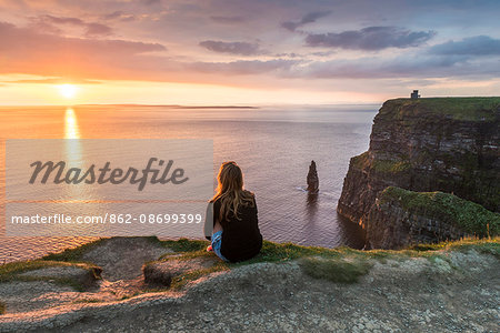 Cliffs of Moher (Aillte an Mhothair), Doolin, County Clare, Munster province, Ireland, Europe. A woman watching the sun setting from the top of the cliff.