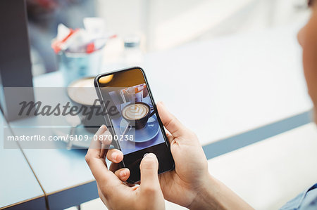 Woman holding mobile phone with photograph of coffee at restaurant