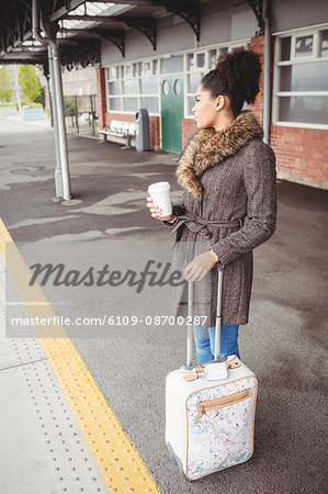 Woman holding disposable coffee cup while standing at railway station platform