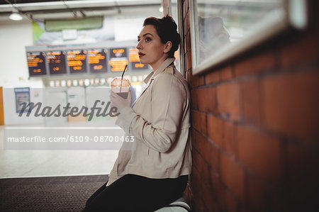 Thoughtful young woman holding drink at railroad station