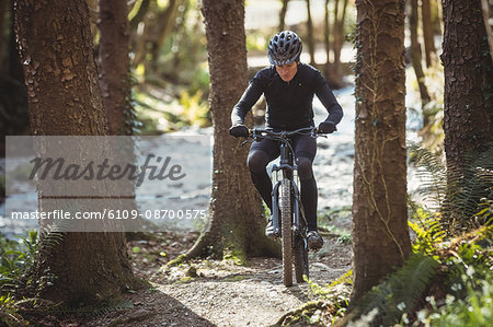 Front view of mountain biker riding by trees in forest