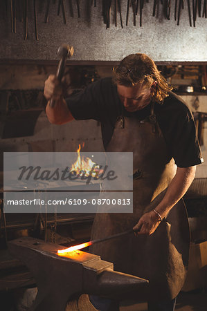 Blacksmith working on hot metal using hammer to shape at work shop