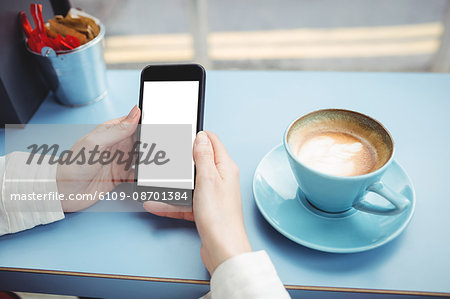 Close-up of woman text messaging on mobile phone in cafeteria