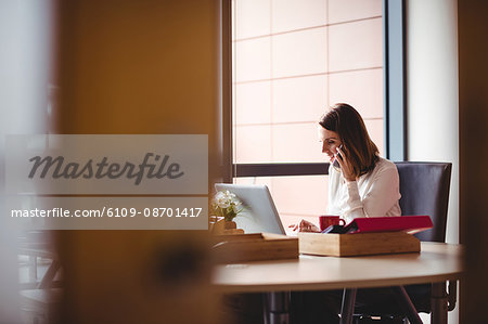 Woman using laptop and talking on mobile phone in the office