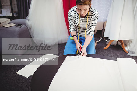 Female fashion designer cutting a white fabric in the studio