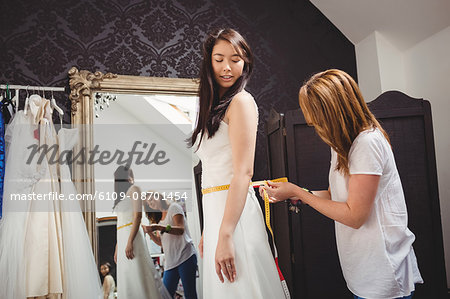 Woman trying on wedding dress in a studio with the assistance of creative designer