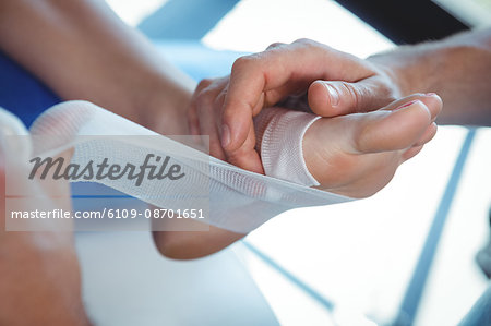 Male therapist putting bandage on female patient foot in clinic