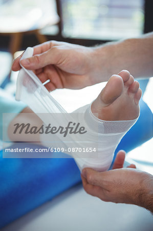 Male therapist putting bandage on female patient foot in clinic