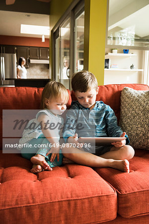 Siblings using digital tablet on sofa
