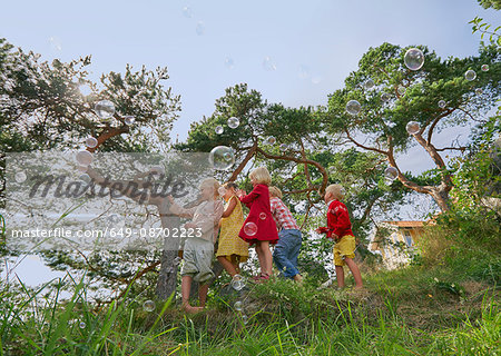 Small group of young friends playing outdoors, watching bubbles in air