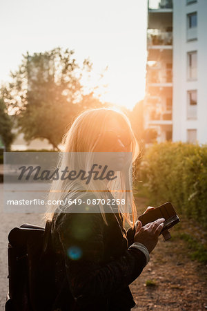 Young woman outdoors, at sunset, using smartphone