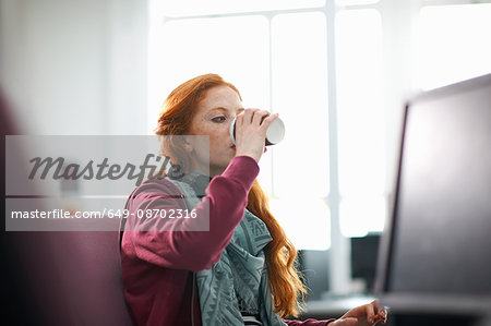 Young female college student at computer desk drinking takeaway coffee