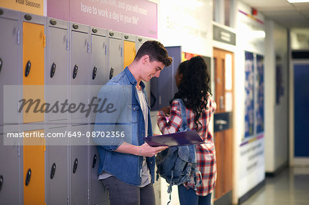 Young male student revising from file in college locker room