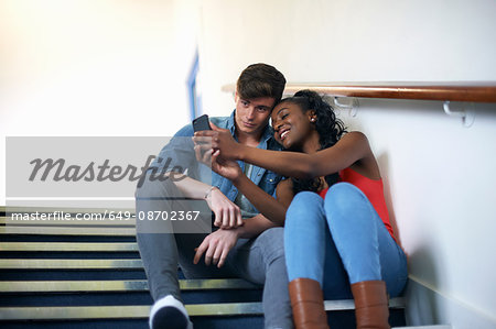 Young college student couple reading smartphone texts on stairway