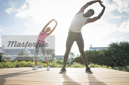 Couple, arms raised bending over sideways stretching