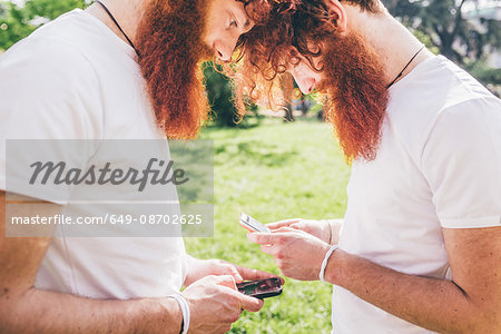 Young male hipster twins with red beards opposite each other texting on smartphones