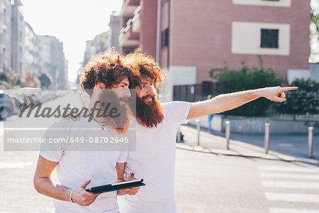 Young male hipster twins with red hair and beards pointing on city street