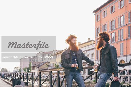 Young male hipster twins with red hair and beards talking on canal waterfront